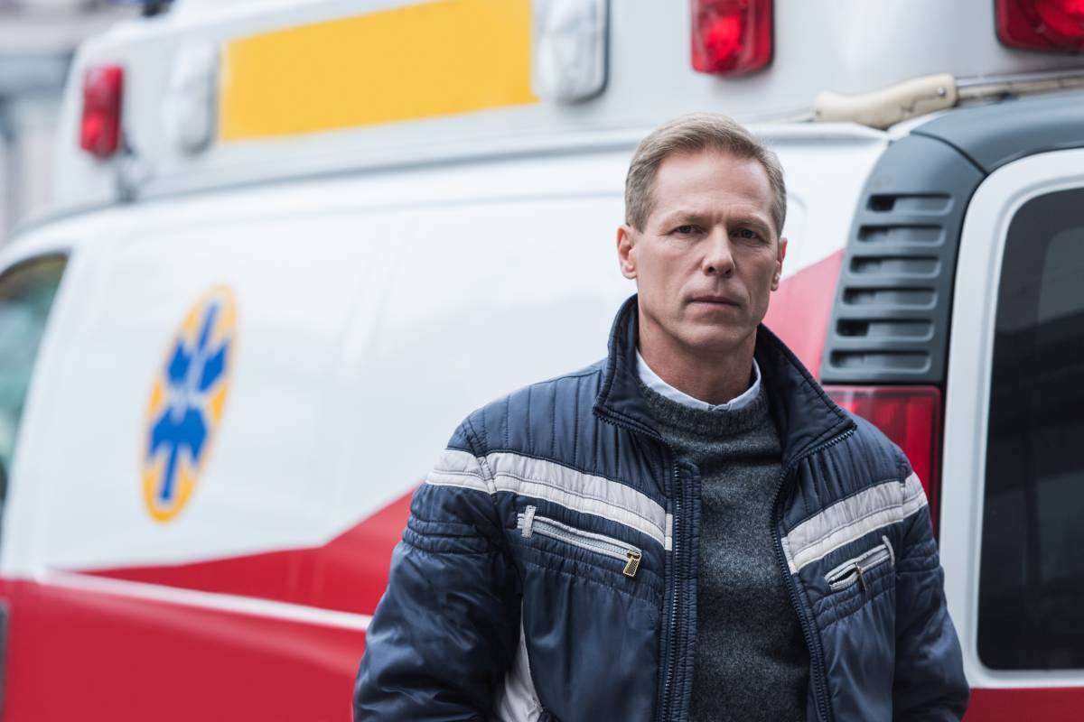 paramedic in casual clothes standing in front of ambulance and looking at camera