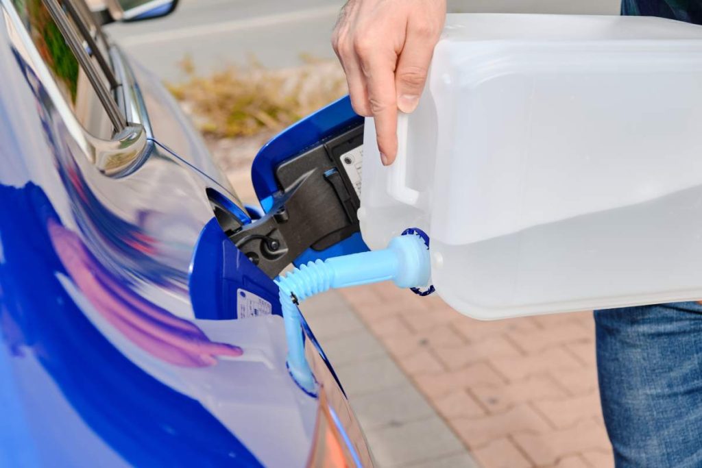 Close up man filling a diesel engine fluid from canister into the tank of blue car. Diesel exhaust fluid for reduction of air pollution. Environmental friendly and eco solution