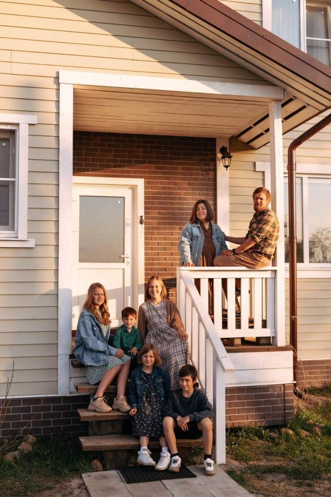 A happy big family sits on the porch of their private white wooden ranch-style house in the summer. The concept of living in a private house or countryside.